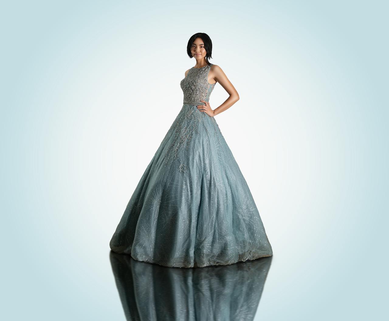 Asian woman elegantly posing in a blue ball gown with a hand on her waist.