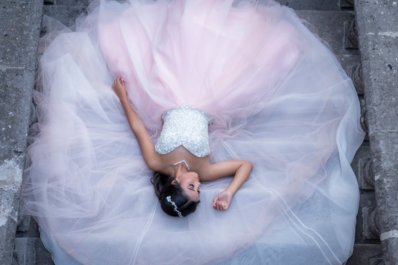 A stunning bride in a beautiful pastel bridal gown lying gracefully on stone stairs.
